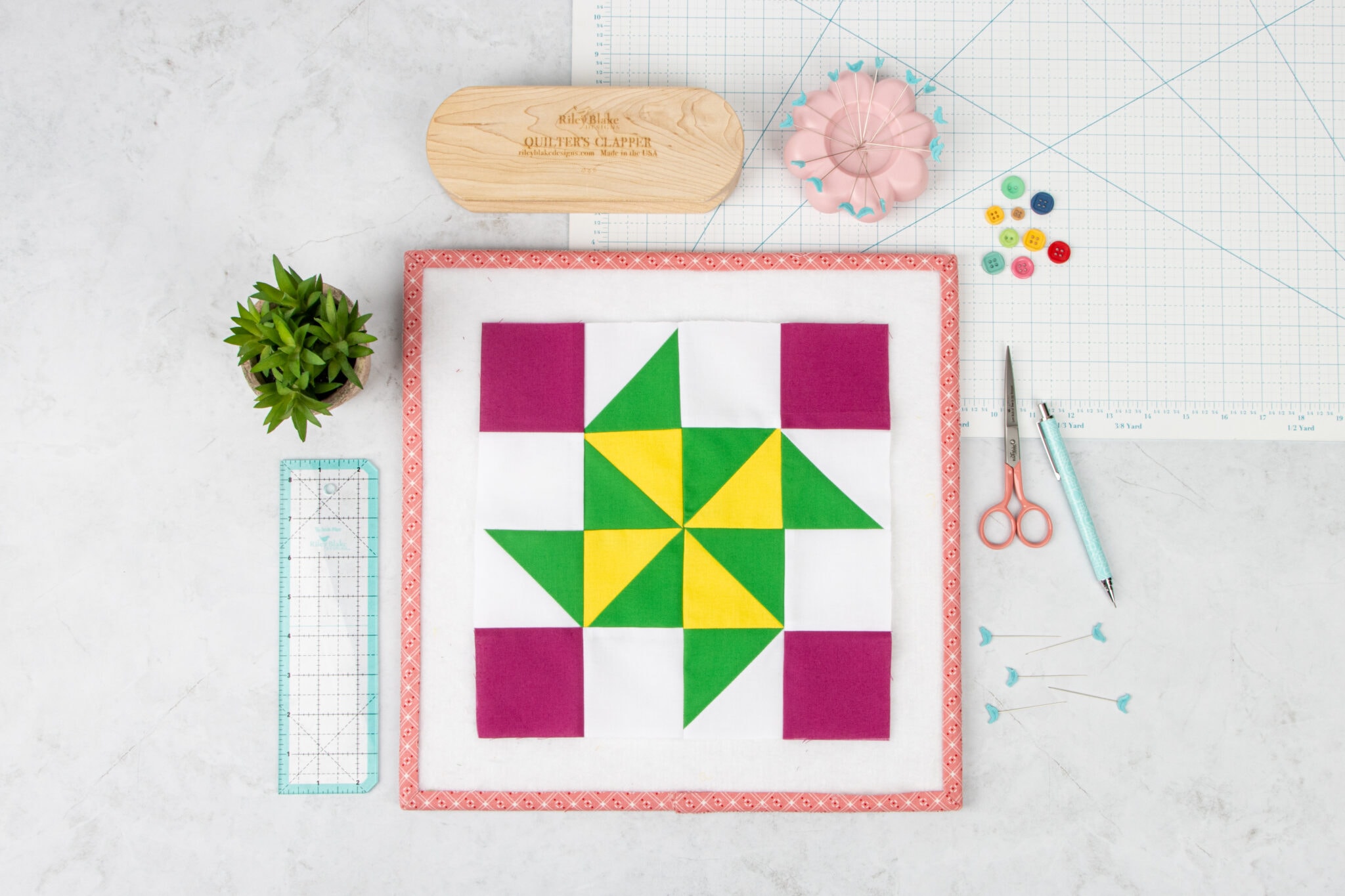 pink, green and yellow quilt block on white table with sewing notions