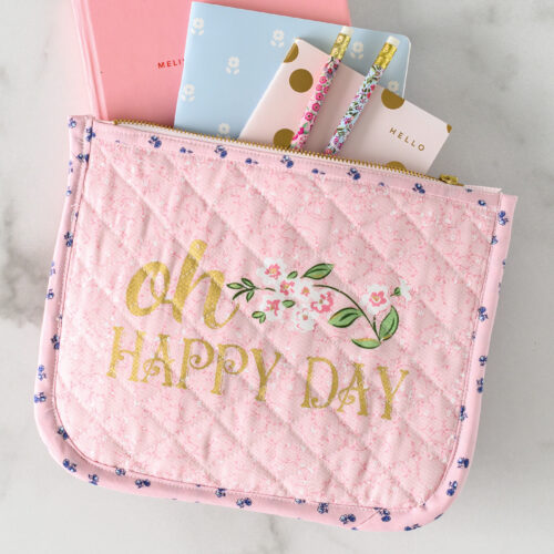 pink quilted zip pouch on white marble table with notebook and pencils