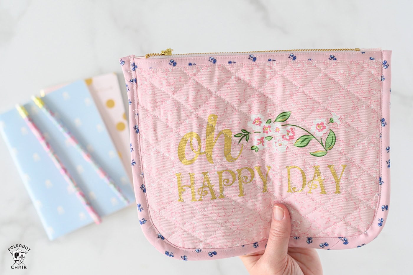 hand holding pink quilted zip pouch on white marble table
