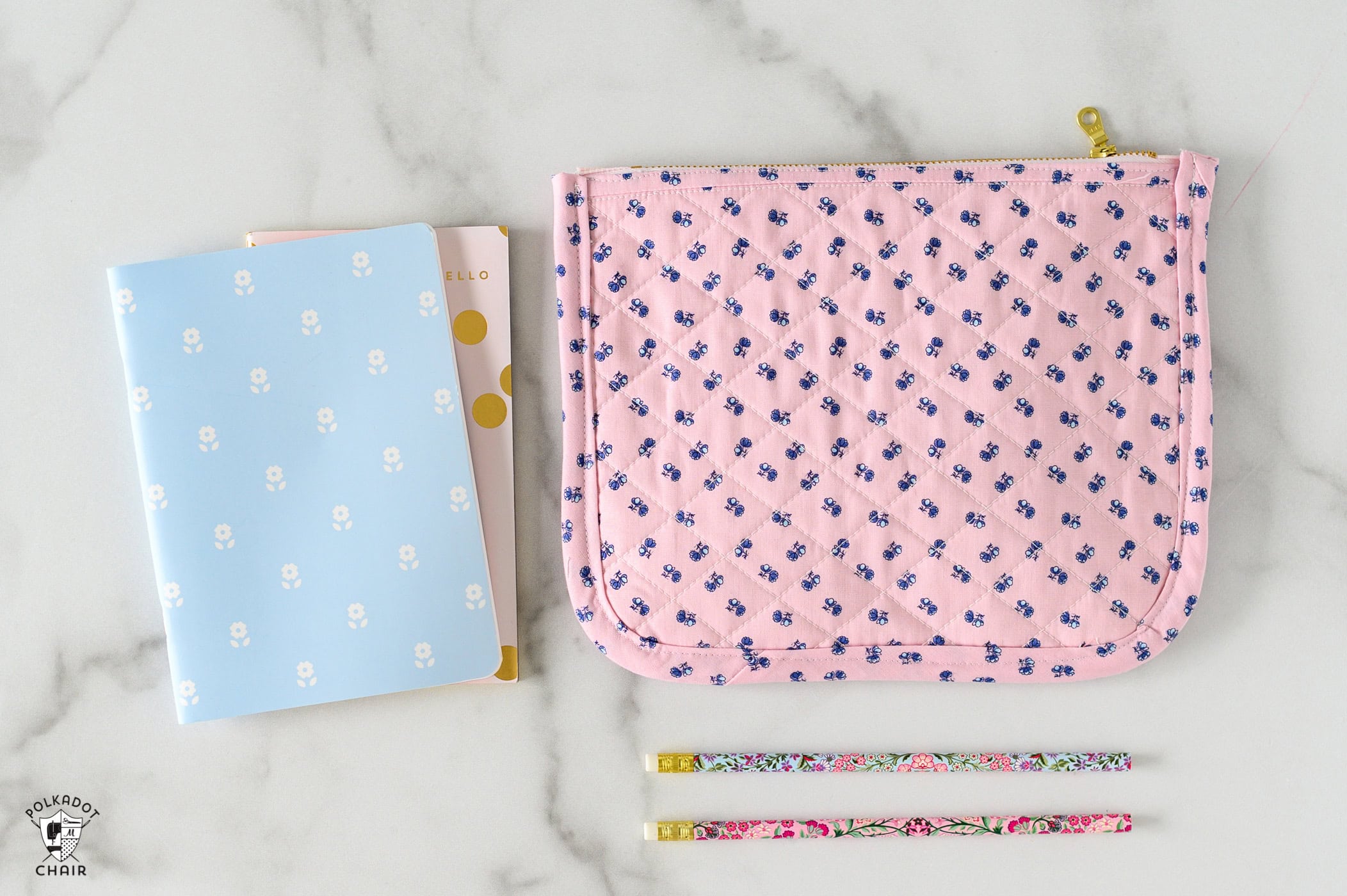 pink quilted zip pouch on white marble table with notebook and pencils