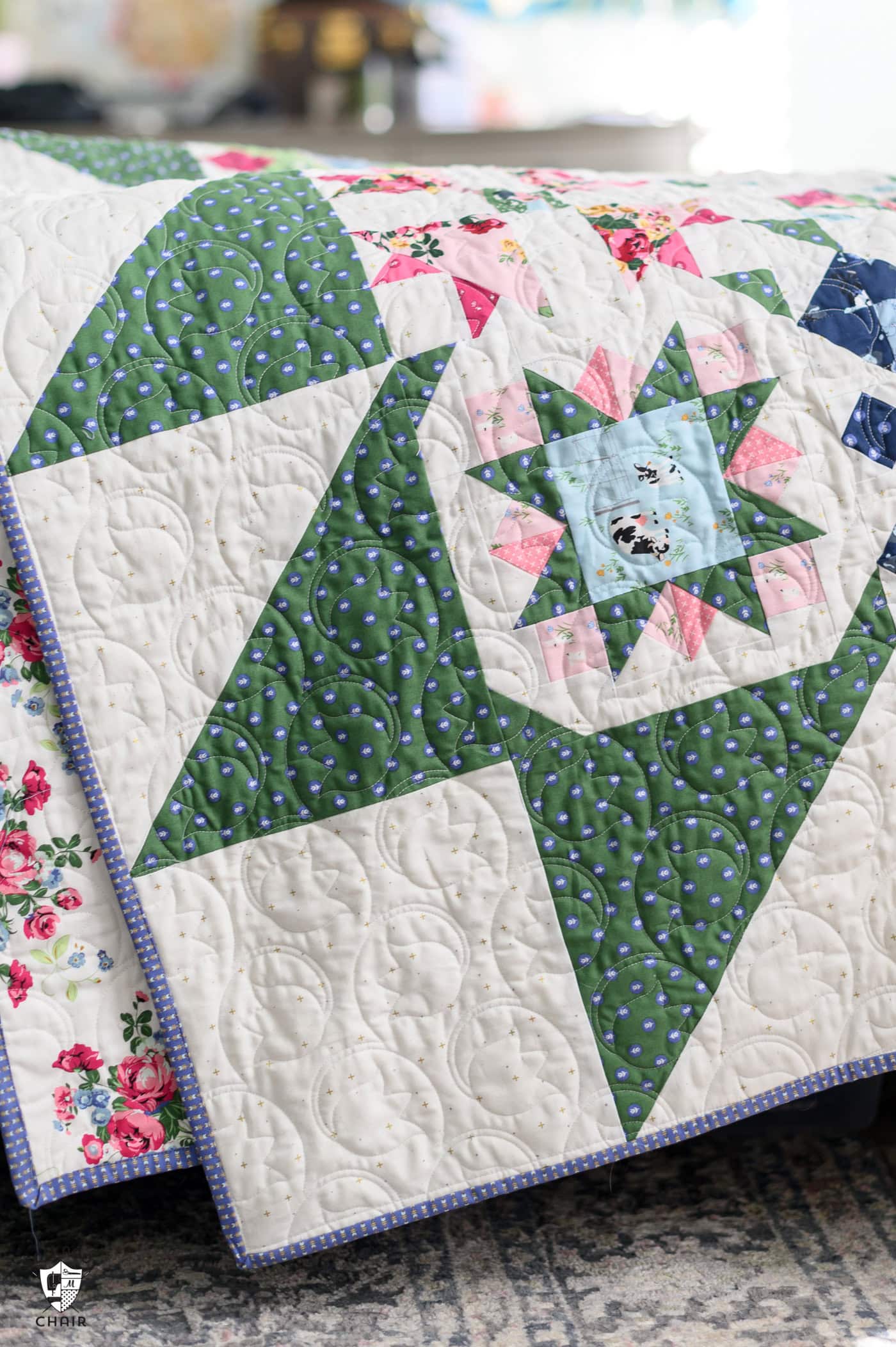 blue, green and pink quilt on bed in bright room