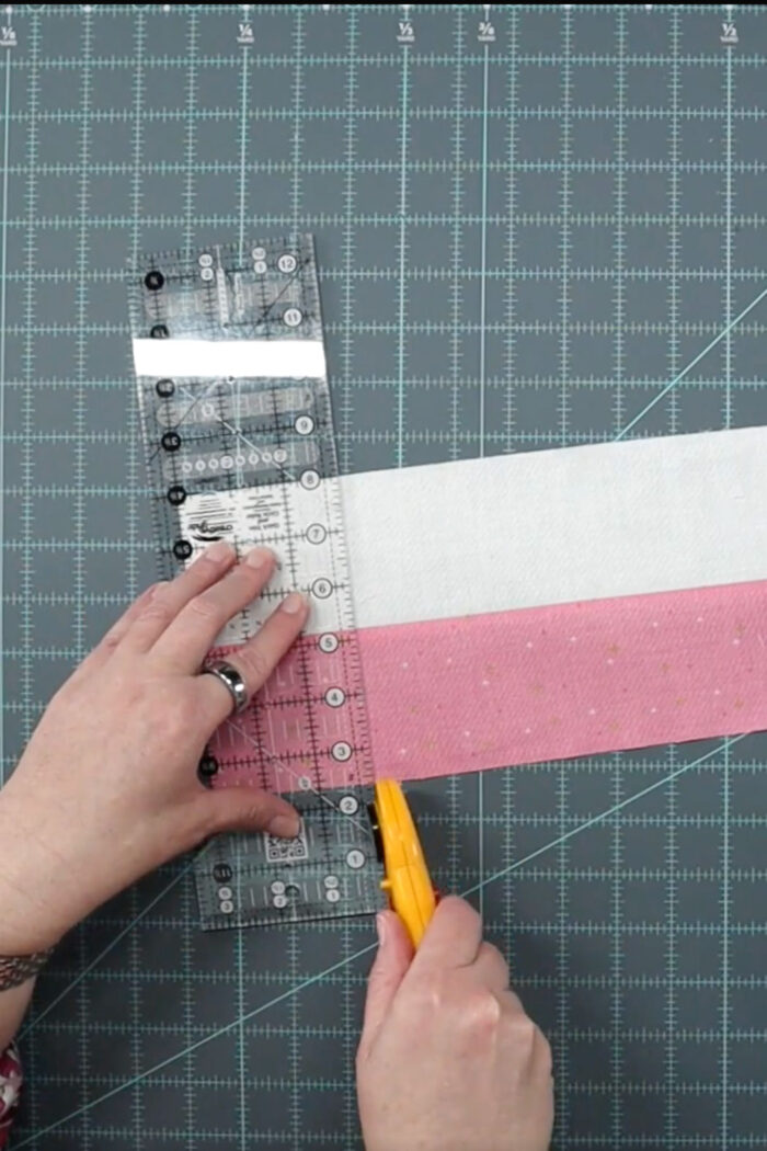 cutting pink and white fabric strip on cutting mat