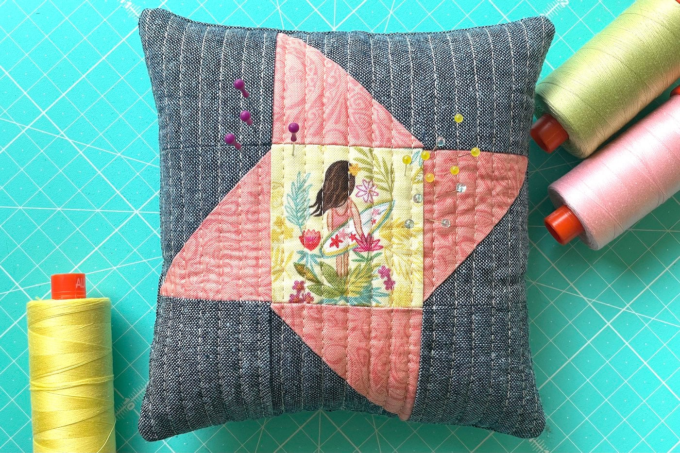 gray and coral pincushion on aqua table with pins and sewing notions