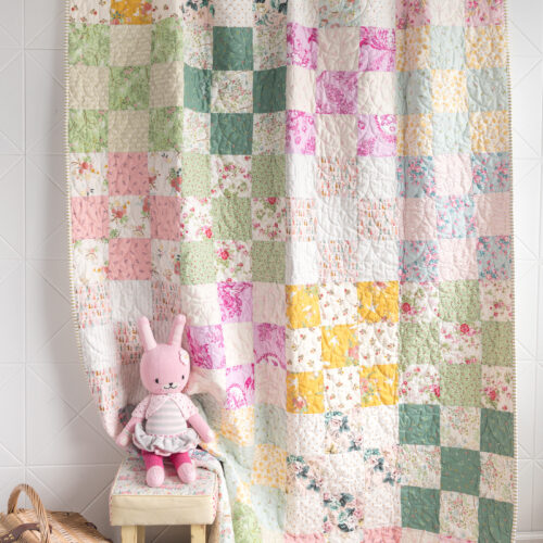 pink, green, yellow and ivory patchwork quilt on wall with toys in the foreground