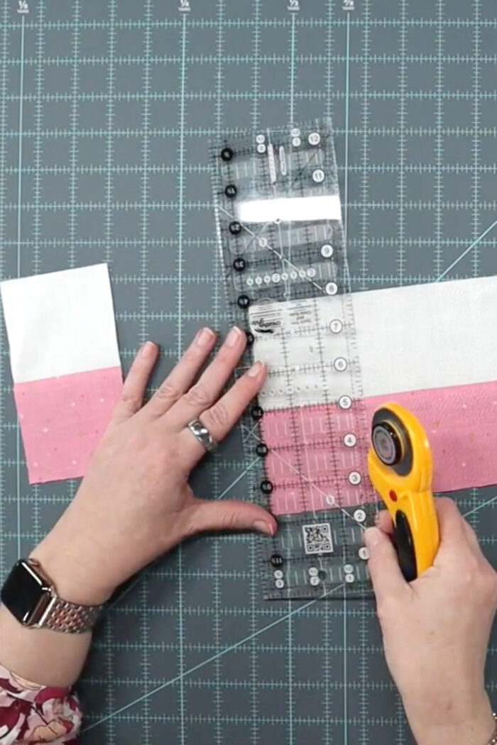 cutting pink and white fabric strip on cutting mat