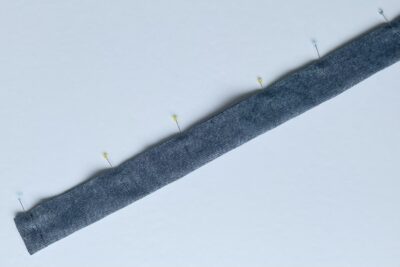 blue fabric strip on white table with pins and thread