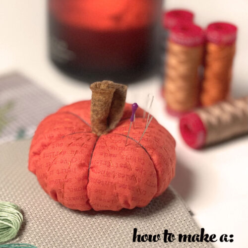 pumpkin pinucushion on table with sewing notions and candle