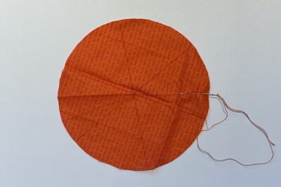 orange circle of fabric on white table, during construction process to turn it into a pumpkin