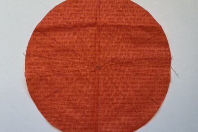 orange circle of fabric on white table, during construction process to turn it into a pumpkin