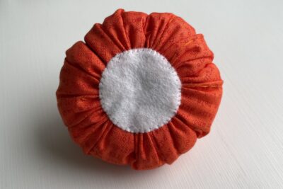 orange circle of fabric on white table, during construction process to turn it into a pumpkin with felt circle on base