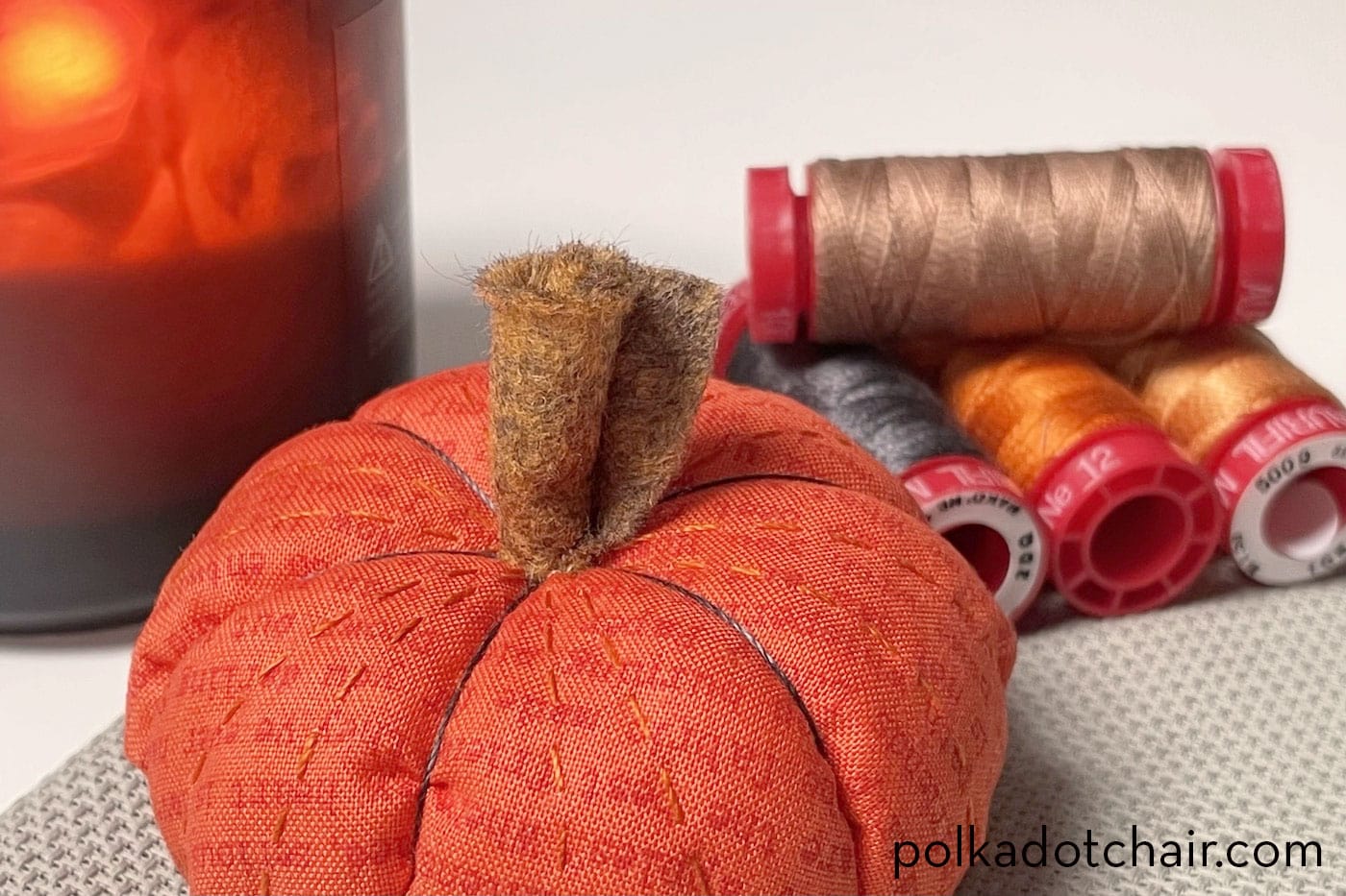 pumpkin pinucushion on table with sewing notions and candle