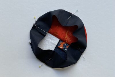 round pincushion construction step on white table with fabric and pins