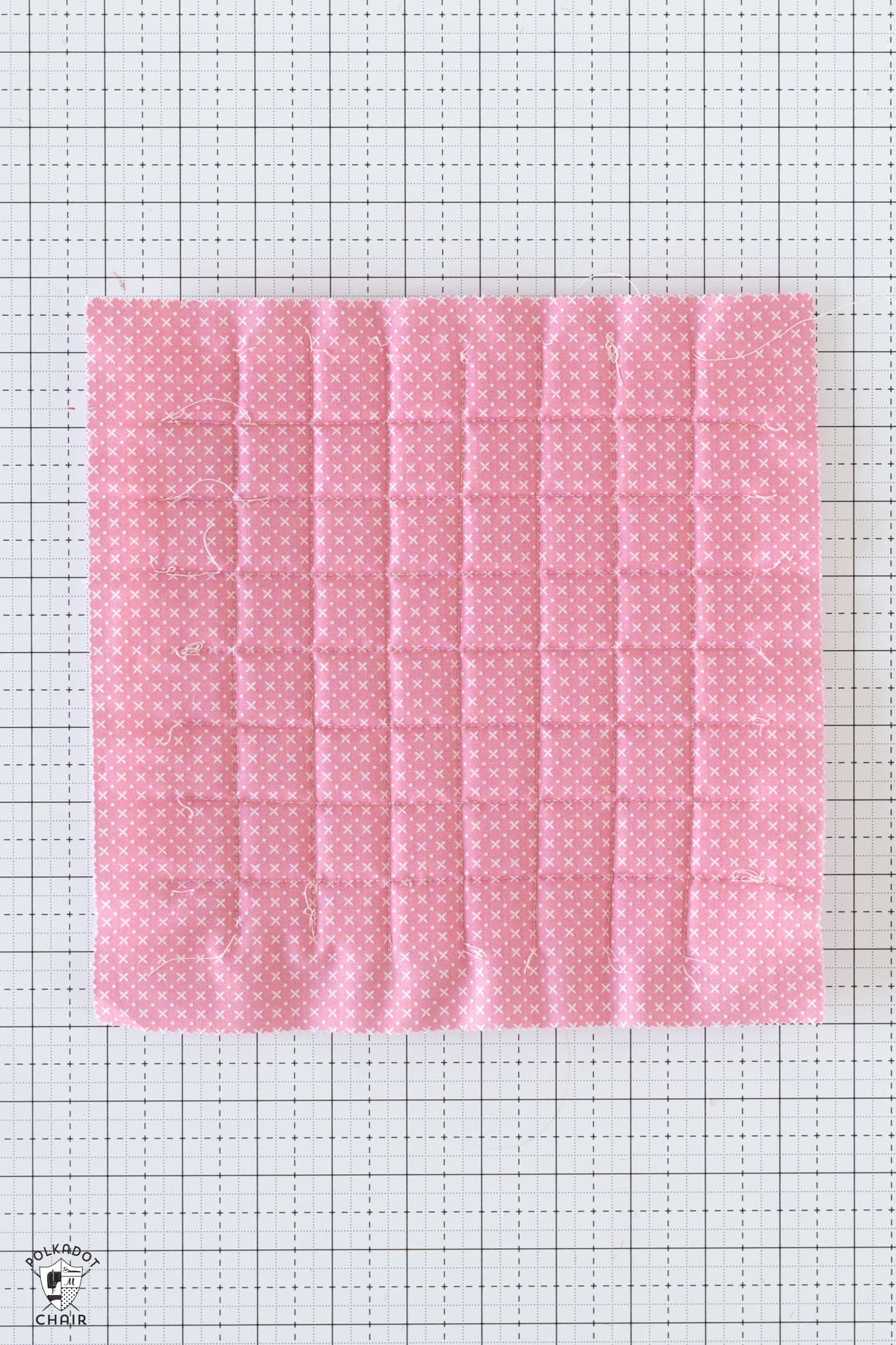 pink square of fabric quilted on white cutting mat