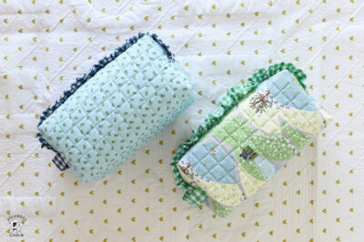 close up of two blue and green ruffle zip pouches on white quilt