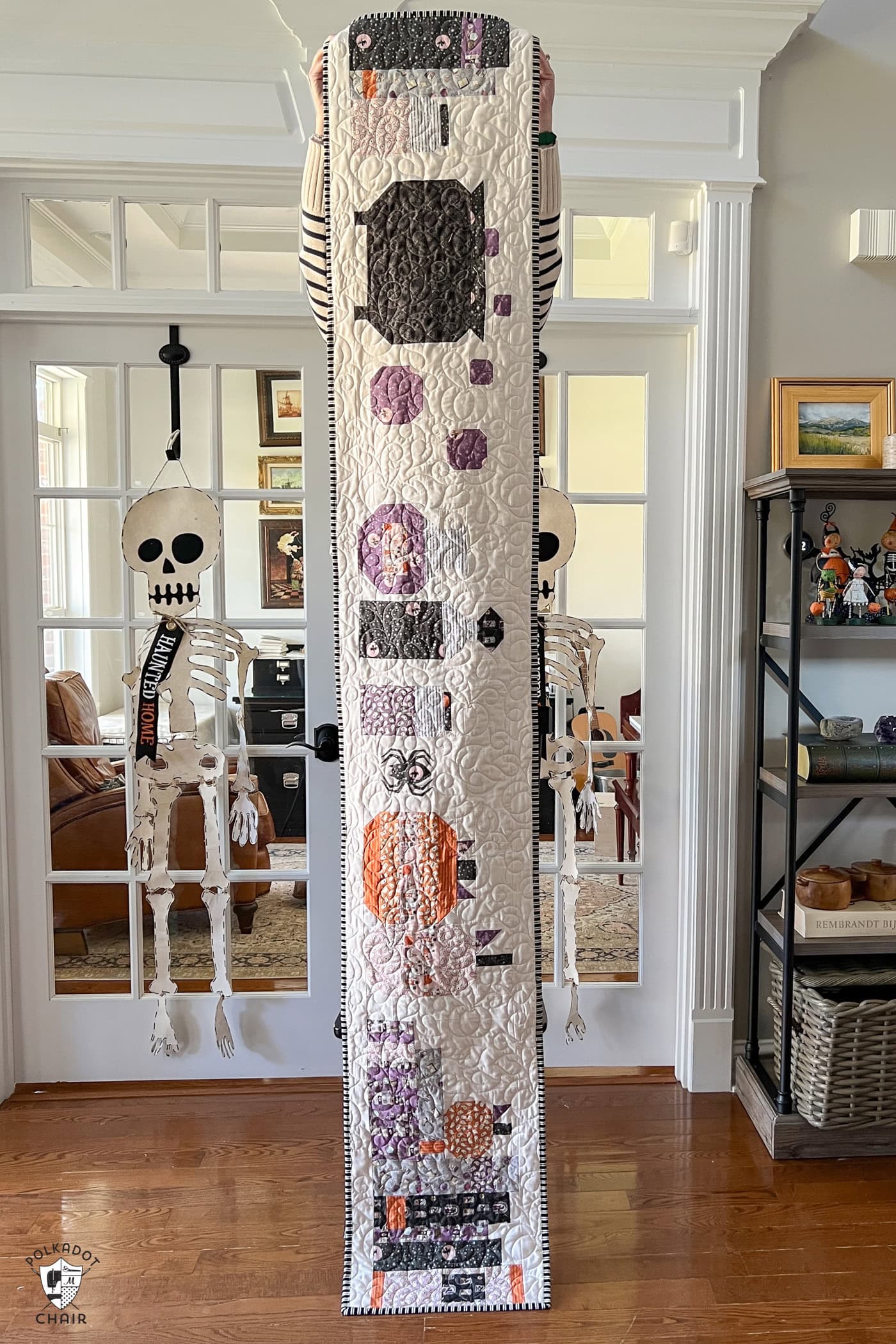 Halloween table runner being held up by woman standing on a chair