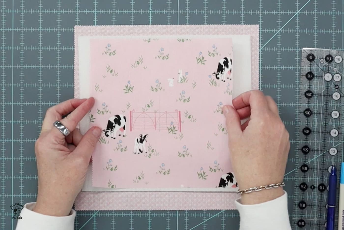 hands holding pink fabric on blue cutting mat