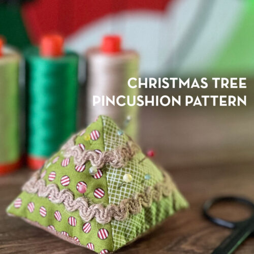 Christmas tree pincushion on wood table with thread in the background
