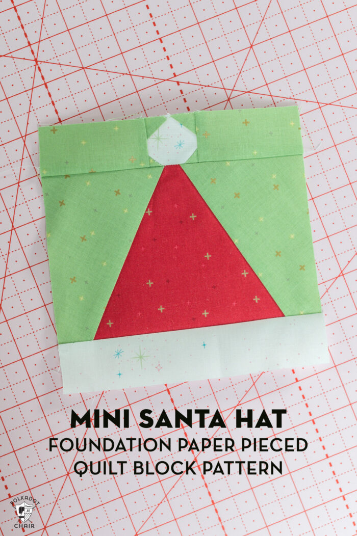 red and white pieced santa claus hat quilt block with green background on pink cutting mat