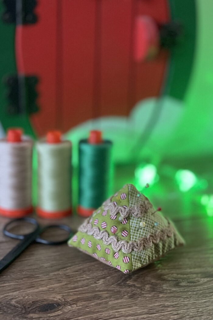 Christmas tree pincushion on wood table with thread in the background