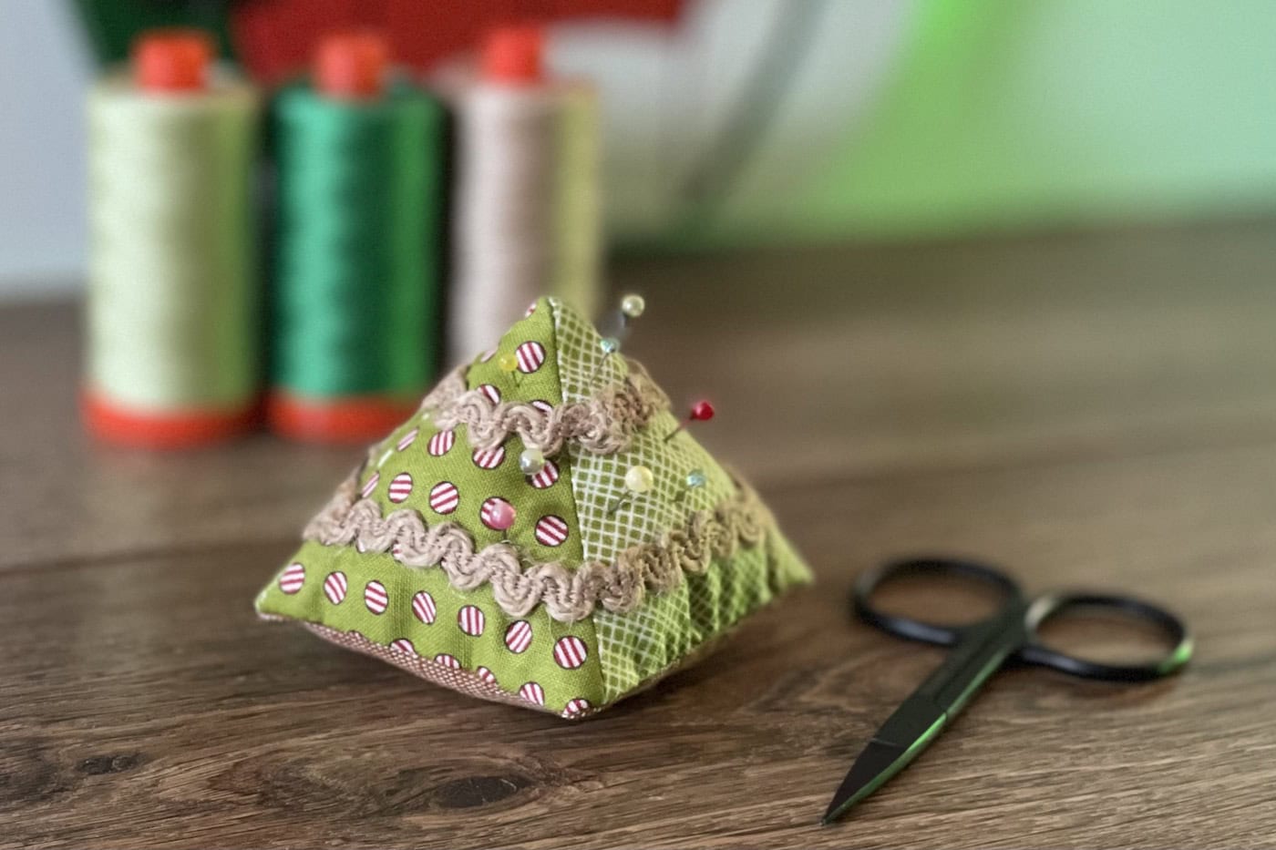 Christmas tree pincushion on wood table with thread in the background