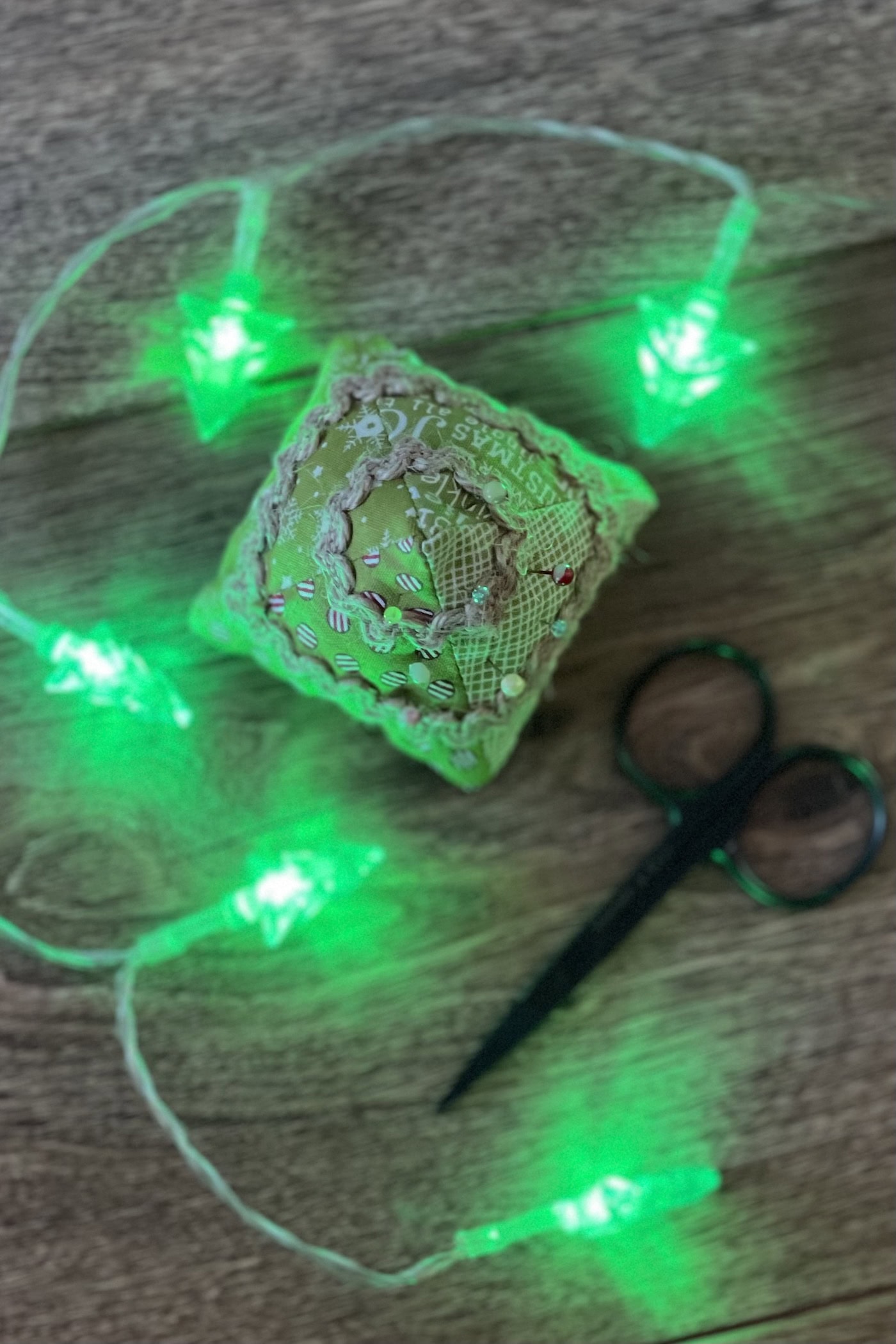 Christmas tree pincushion on wood table with thread in the background