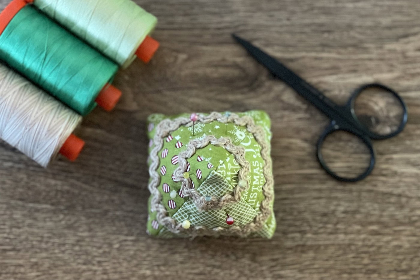 Christmas tree pincushion on wood table with thread in the background