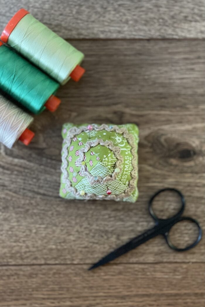 Christmas tree pincushion on wood table with thread in the background