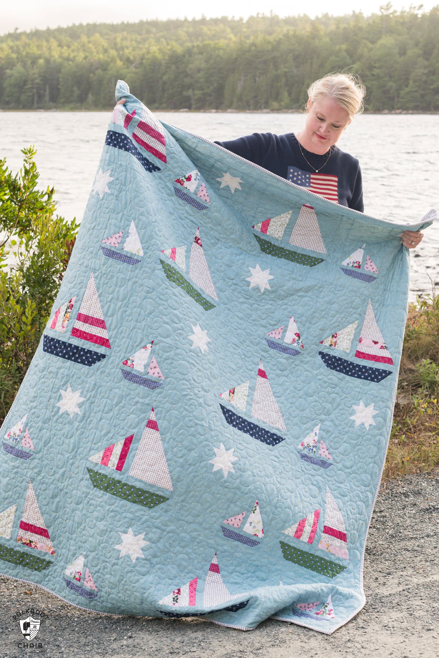 woman holding Blue quilt with white, red and green sailboat quilt blocks outdoors
