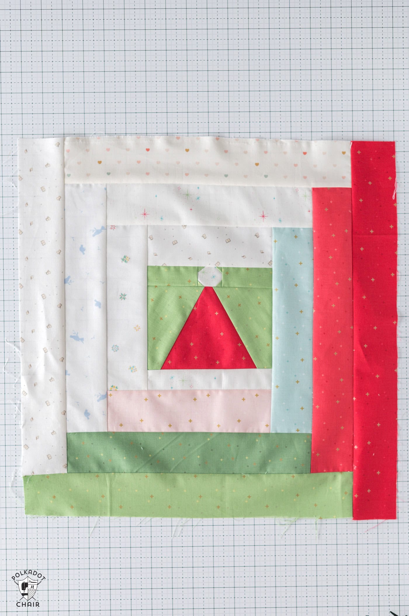 red and white pieced santa claus hat quilt block with green background surrounded by strips of white, green, red and blue fabric