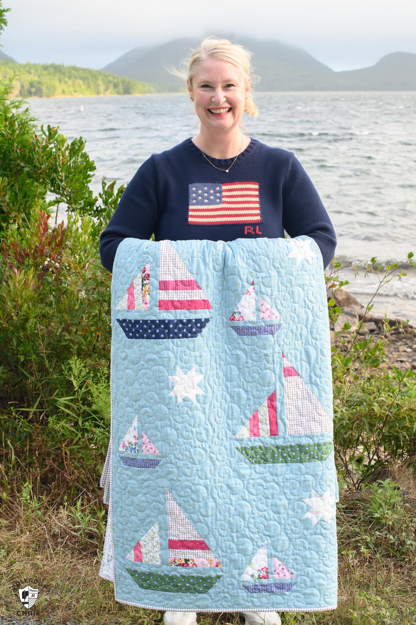 woman holding Blue quilt with white, red and green sailboat quilt blocks outdoors