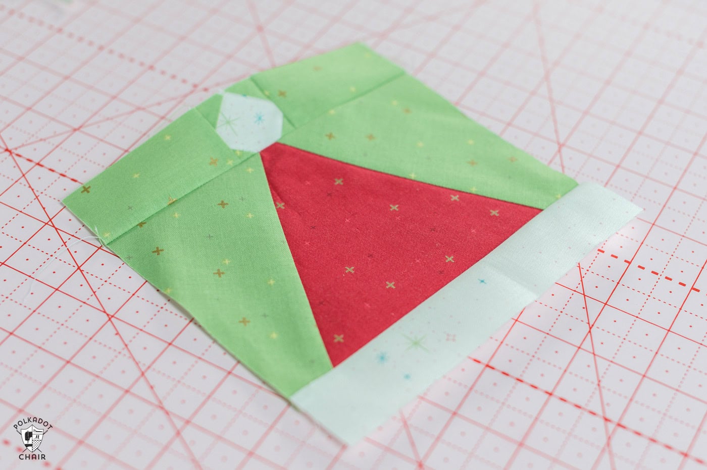 red and white pieced santa claus hat quilt block with green background on pink cutting mat
