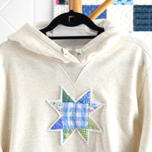 cream sweatshirt with quilt block on front in front of patchwork quilt