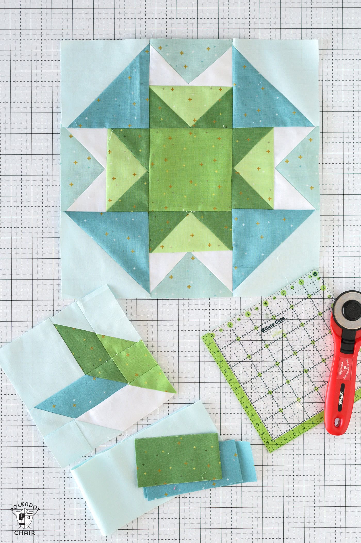 Blue and green quilt blocks on white cutting mat with quilt ruler and rotary cutter