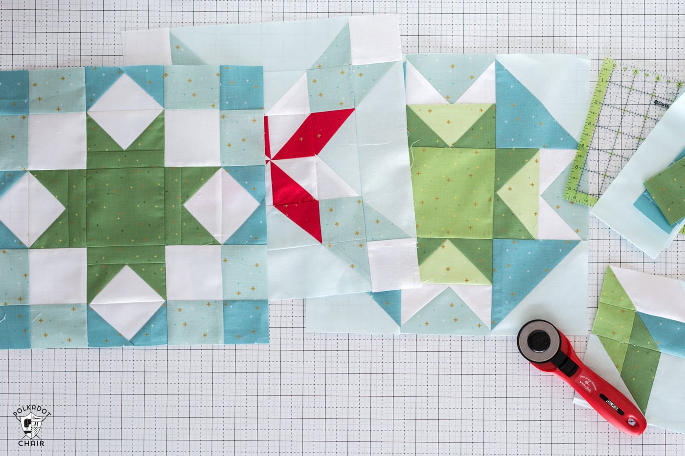 Blue and green quilt blocks on white cutting mat with quilt ruler and rotary cutter