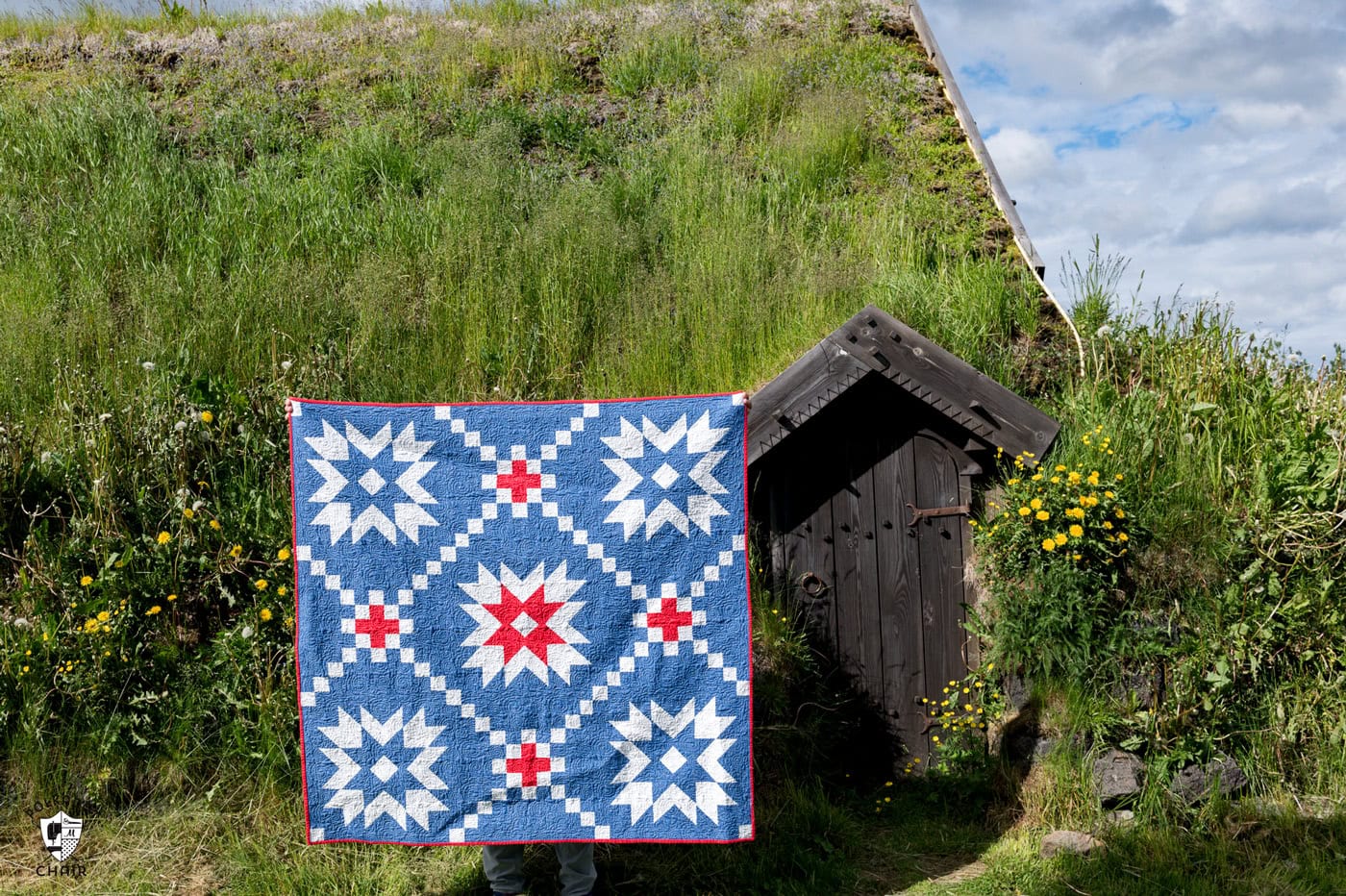 blue and red quilt in front of moss covered home