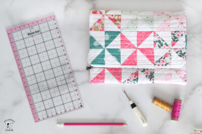 Pink aqua and blue quilted zip pouch with sewing accessories on white table