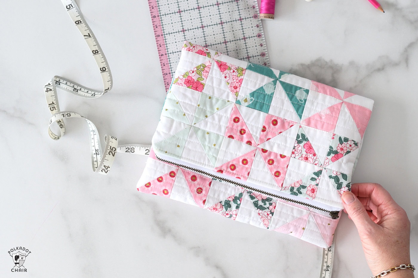 Pink aqua and blue quilted zip pouch with sewing accessories on white table