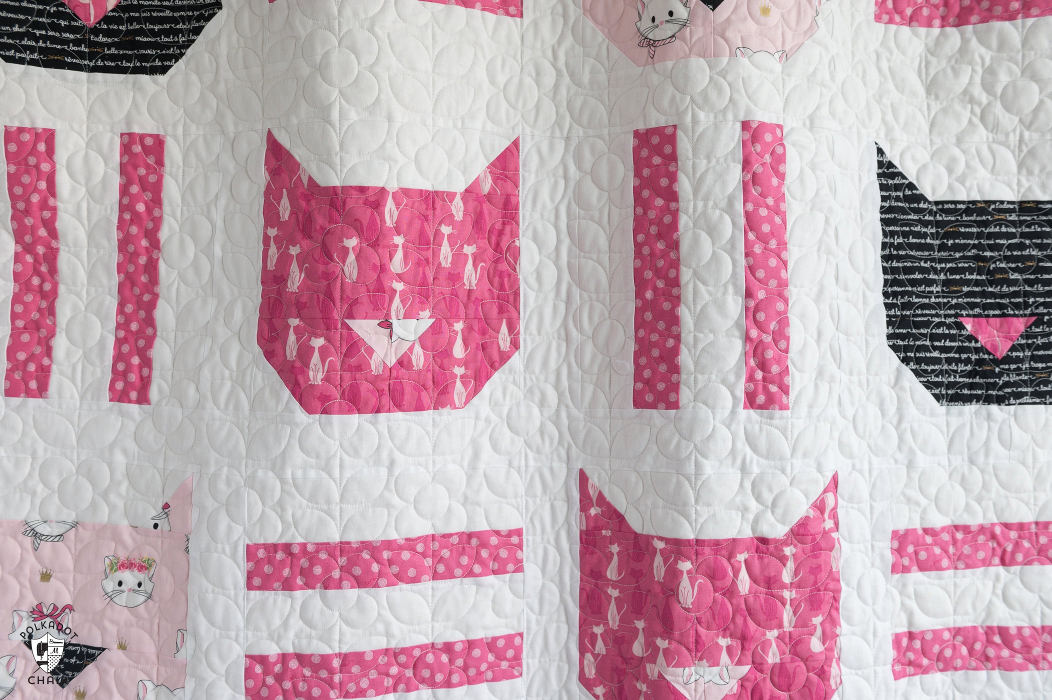 Pink, white and black cat quilt hanging on white wall