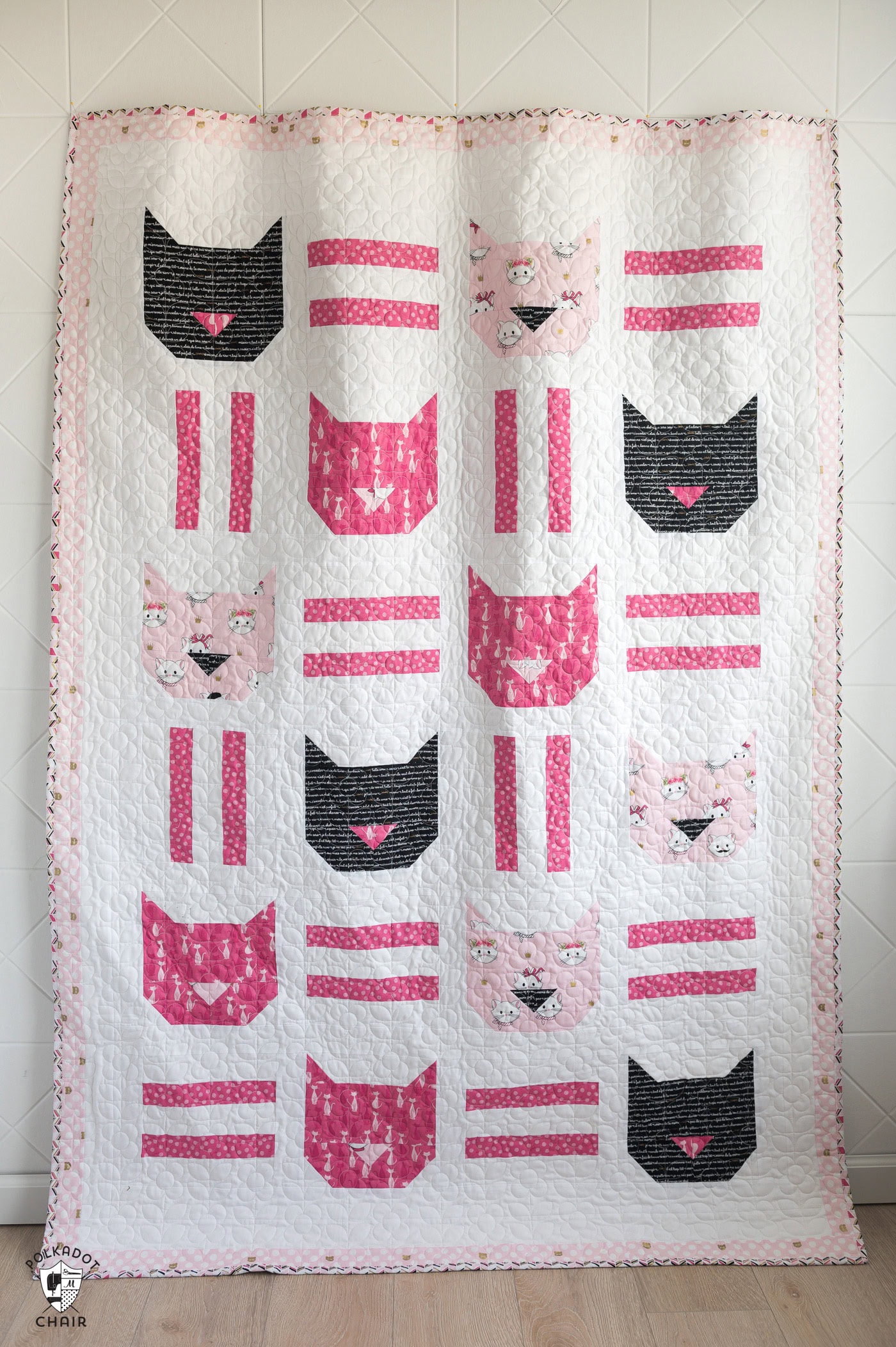 Pink, white and black cat quilt hanging on white wall