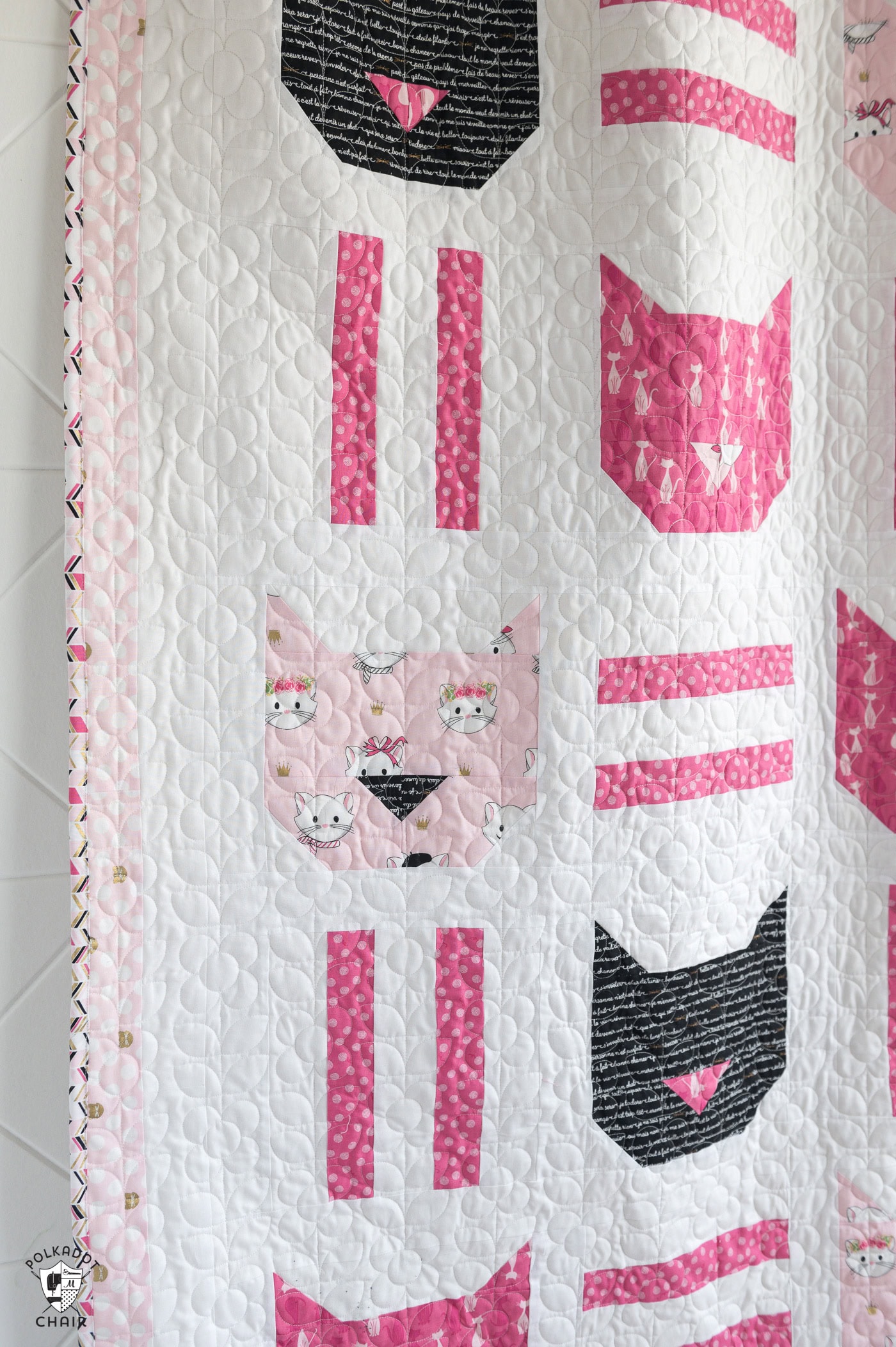 Pink, white and black cat quilt hanging on white wall