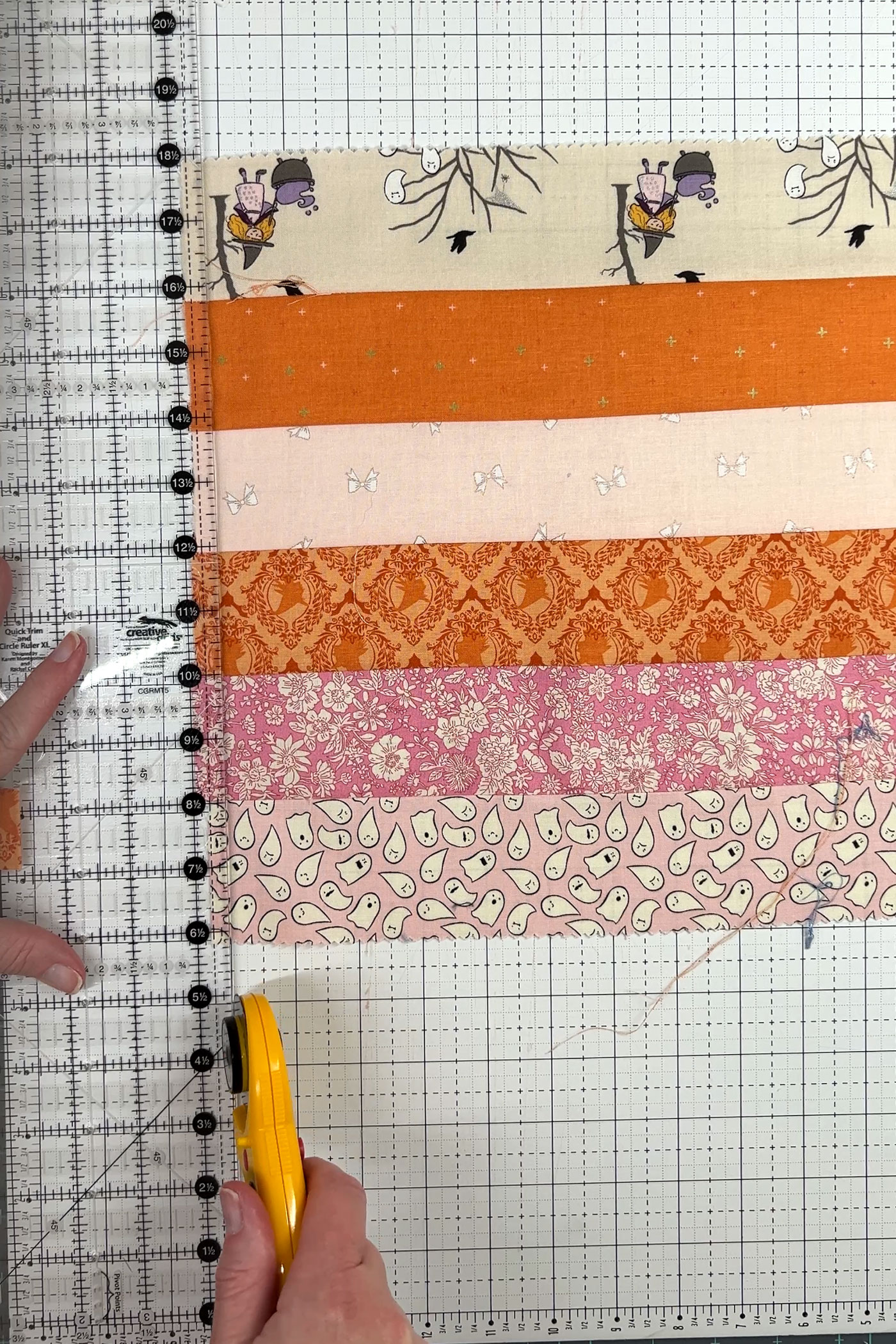 orange, pink and ivory strips of fabric being cut with rotary cutter and ruler