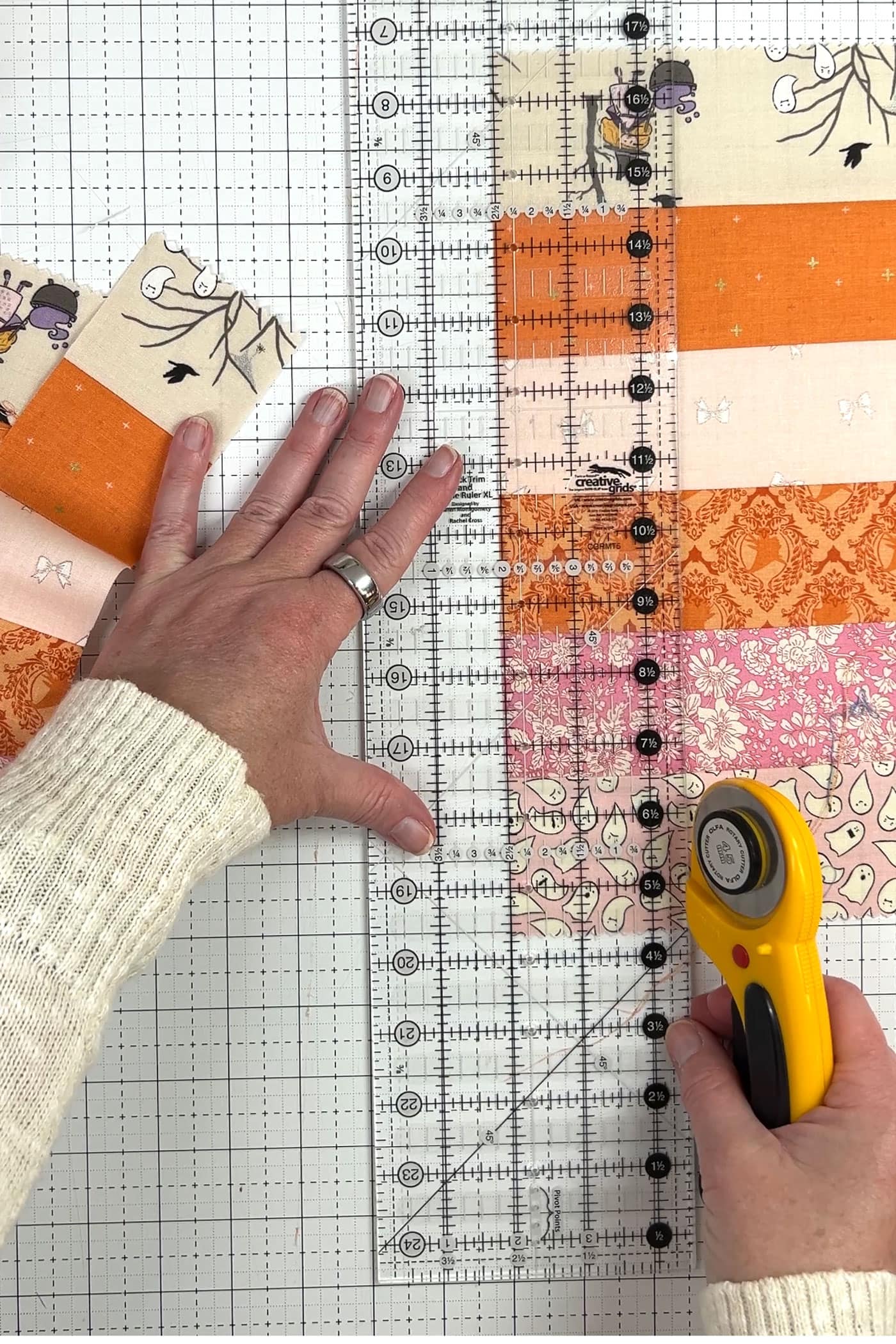 orange, pink and ivory strips of fabric being cut with rotary cutter and ruler