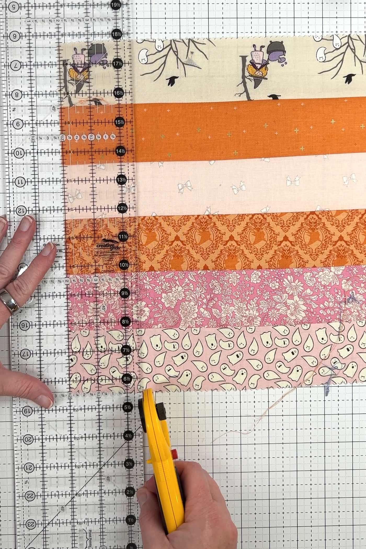 orange, pink and ivory strips of fabric being cut with rotary cutter and ruler