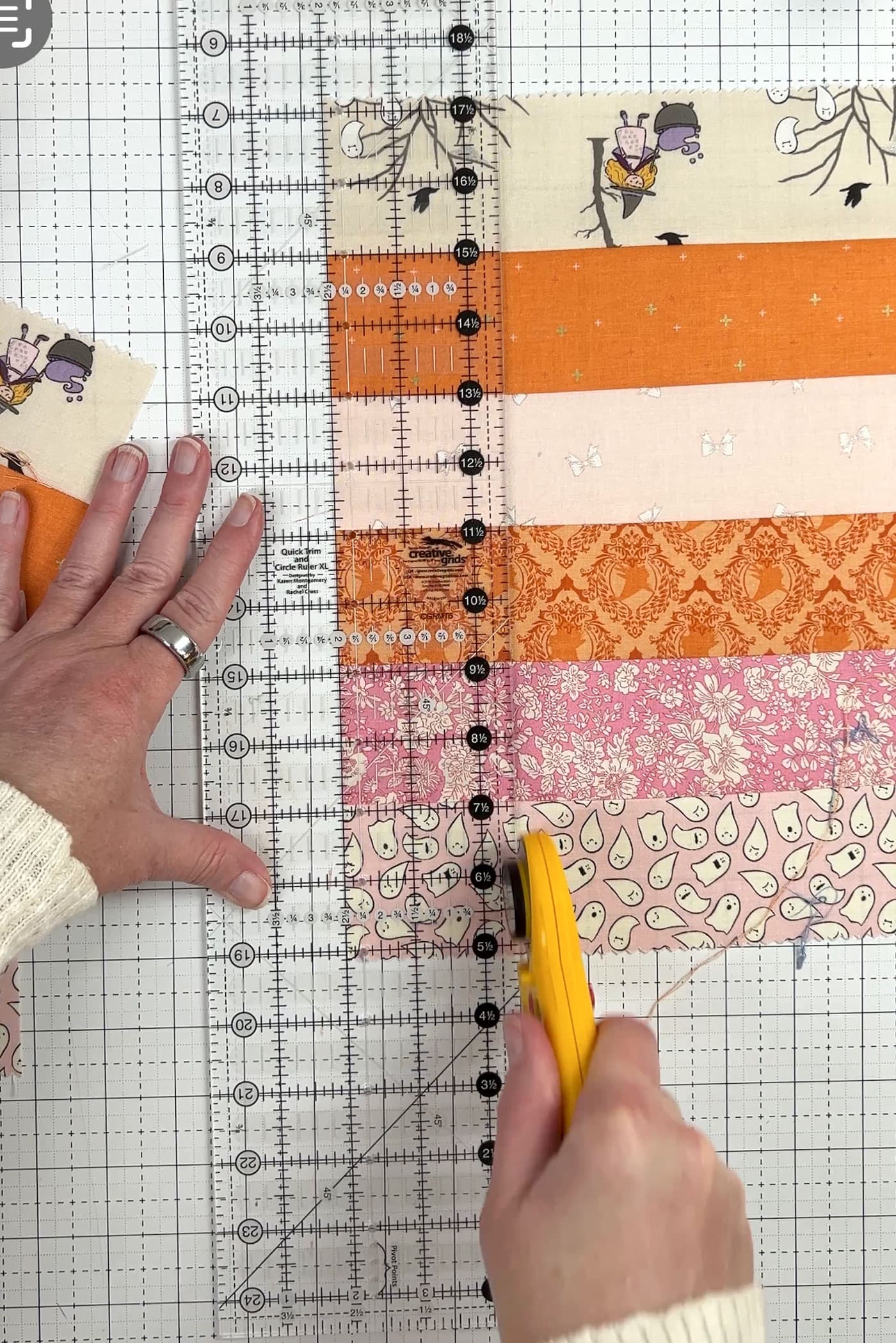 orange, pink and ivory strips of fabric being cut with rotary cutter and ruler