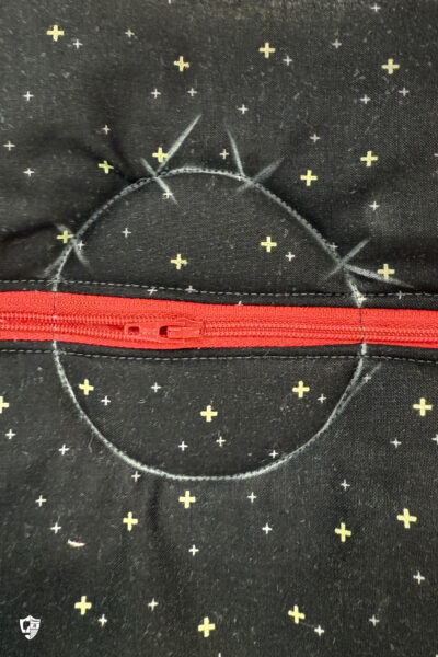 black fabric on cutting mat with red zipper showing construction steps of zip pouch