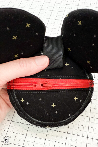 black fabric on cutting mat with red zipper showing construction steps of zip pouch