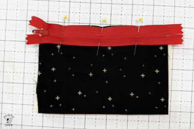 black fabric on cutting mat with red zipper showing construction steps of zip pouch