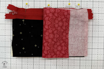 black fabric on cutting mat with red zipper showing construction steps of zip pouch