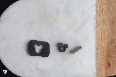 marble slab with black clay rolled out, mickey head cut out of the clay slab and a hole cut out of the mickey head shaped piece of clay.