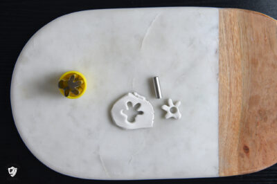 white clay rolled out, with glove shaped cookie cutter and glove shape cuto ut of clay. with hole in the middle of the cut out glove.
